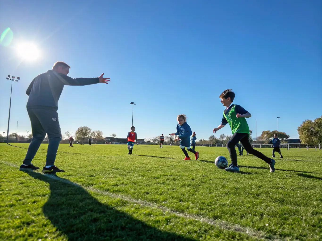 A vibrant outdoor scene showing children and teenagers playing soccer on a well-maintained community field, with AXELSAAT coaches providing guidance and encouragement, under a clear sky, capturing the energy and inclusivity of youth sports.